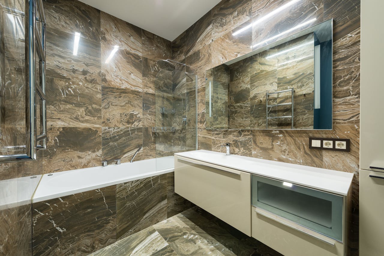 Bathtub placed near wall sink on cabinet at wall with mirror placed in contemporary bathroom with marble tiles at home